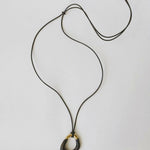 Momentum Necklace in black and gold by Enso Design Lab, displayed flat with a vegan leather cord. The pendant's unique, liquid-inspired design is highlighted with enamel and gold plating.