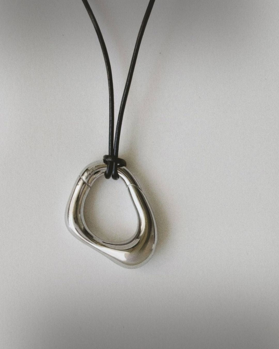 Momentum Necklace in silver color by Enso Design Lab, displayed flat with a leather cord. The pendant's unique, liquid-inspired design is clearly visible.