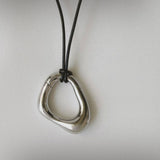 Momentum Necklace in silver color by Enso Design Lab, displayed flat with a leather cord. The pendant's unique, liquid-inspired design is clearly visible.