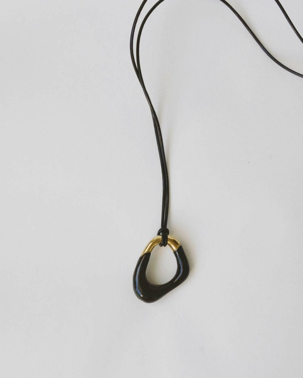 Momentum Necklace in black and gold, hanging on a vegan leather cord. Designed by Ani Han, this piece combines modern elegance with minimalism, featuring enamel coating and 18K gold plating.