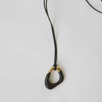 Momentum Necklace in black and gold, hanging on a vegan leather cord. Designed by Ani Han, this piece combines modern elegance with minimalism, featuring enamel coating and 18K gold plating.