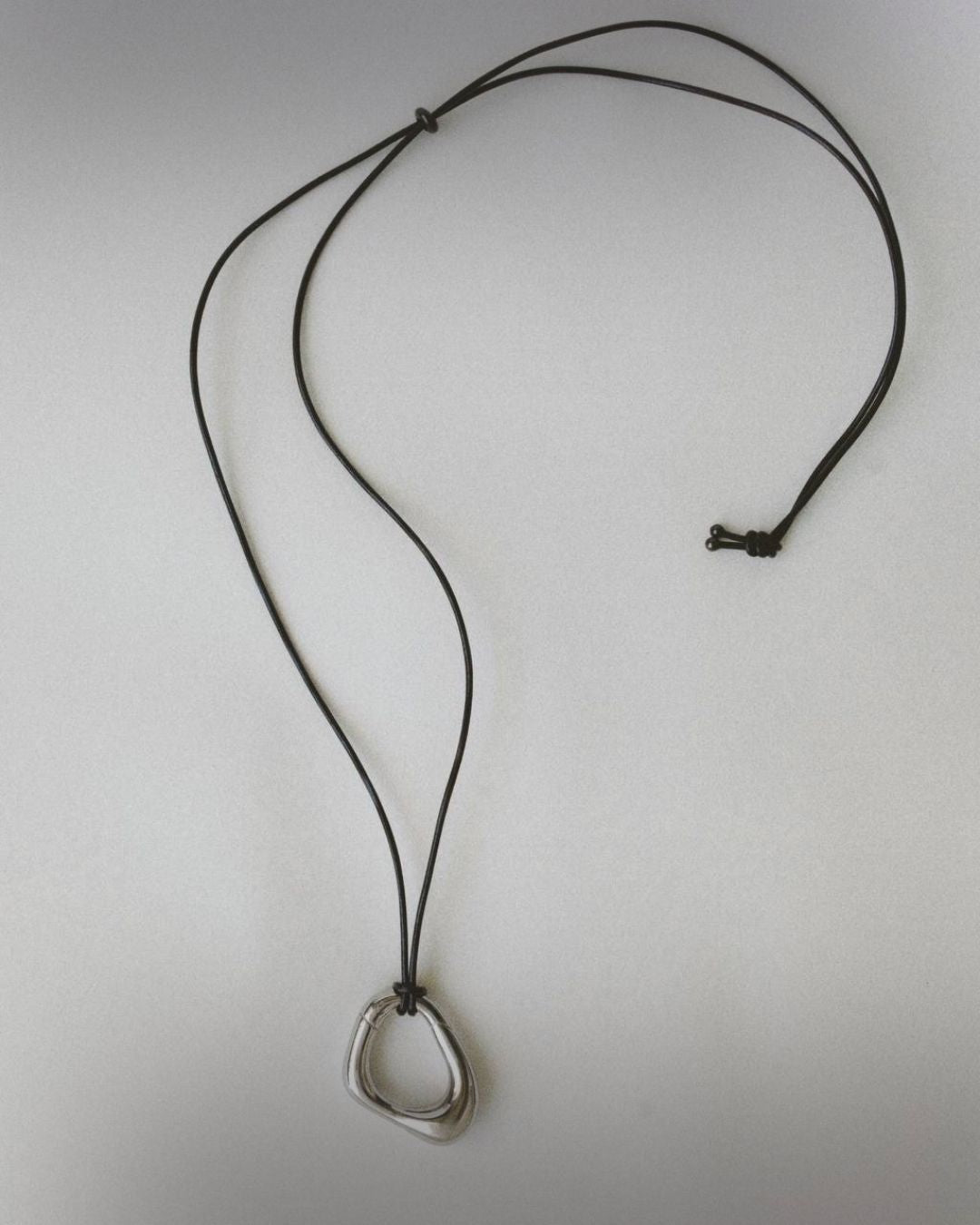 Momentum Necklace by Enso Design Lab, featuring a unique, fluid-inspired pendant in silver color. The necklace is laid flat with the leather cord visible.