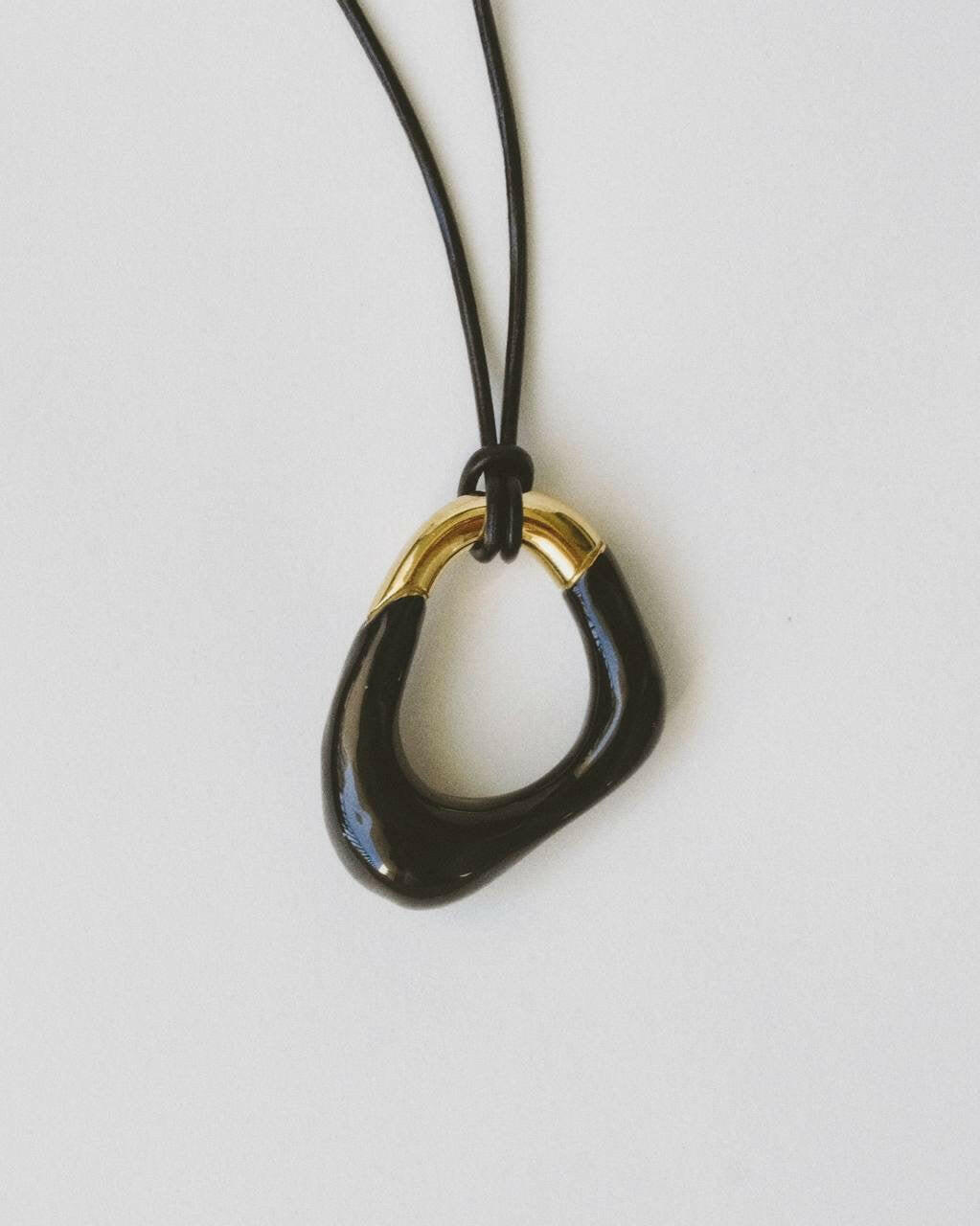 Momentum Necklace in black and gold, designed by Ani Han, laid flat. The pendant's unique shape symbolizes the fluidity of life, with enamel coating and 18K gold plating.