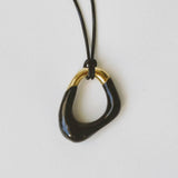 Momentum Necklace in black and gold, designed by Ani Han, laid flat. The pendant's unique shape symbolizes the fluidity of life, with enamel coating and 18K gold plating.