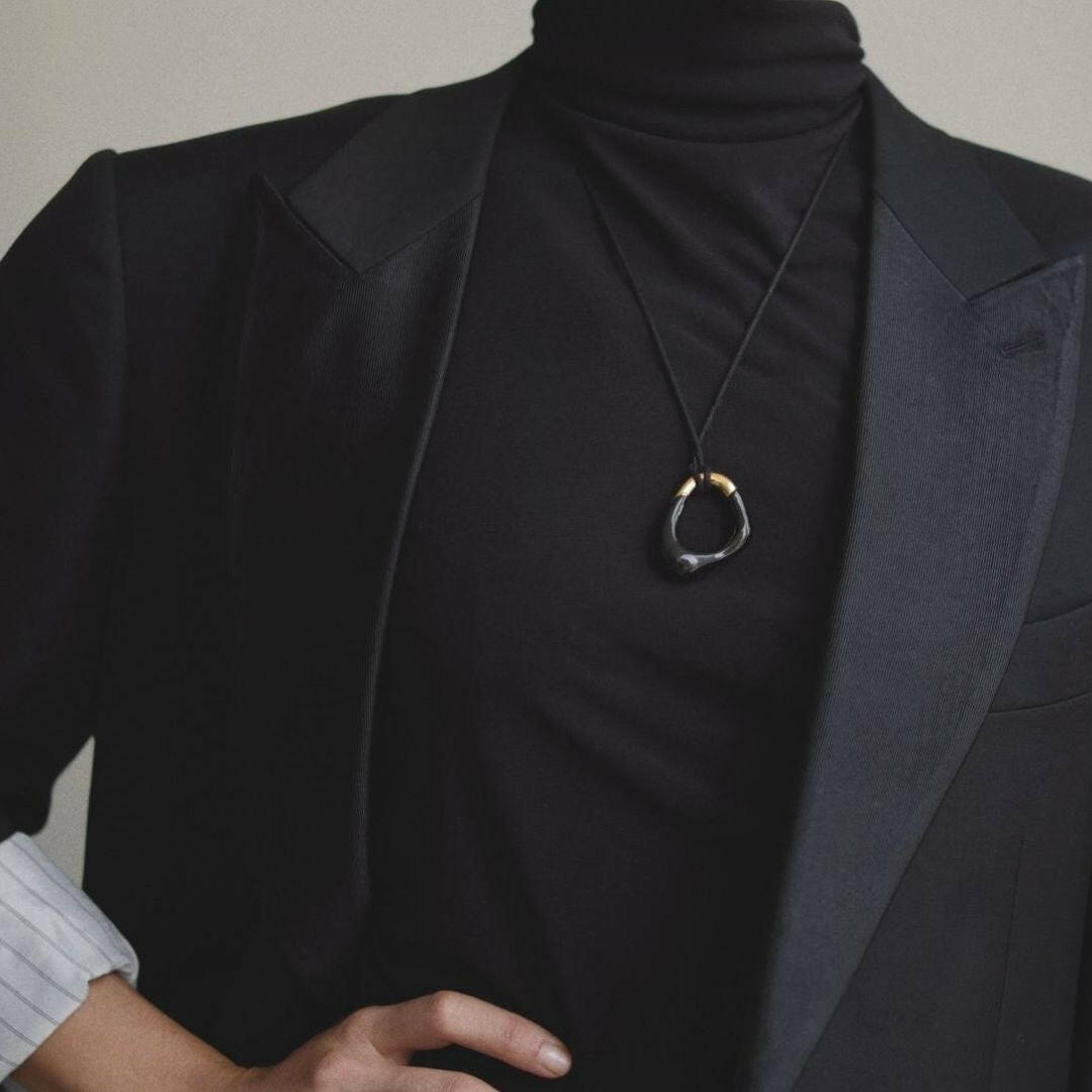 Model wearing the Momentum Necklace in black and gold, paired with a black blazer. The pendant stands out as a statement piece, featuring enamel coating and 18K gold plating.