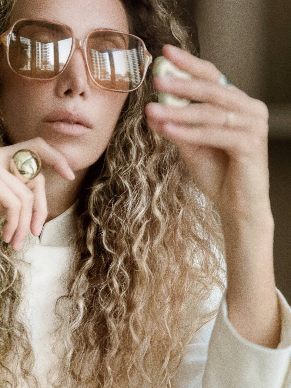 Ani Han wearing gold sunglasses and a ring, holding a phone with a blurred background