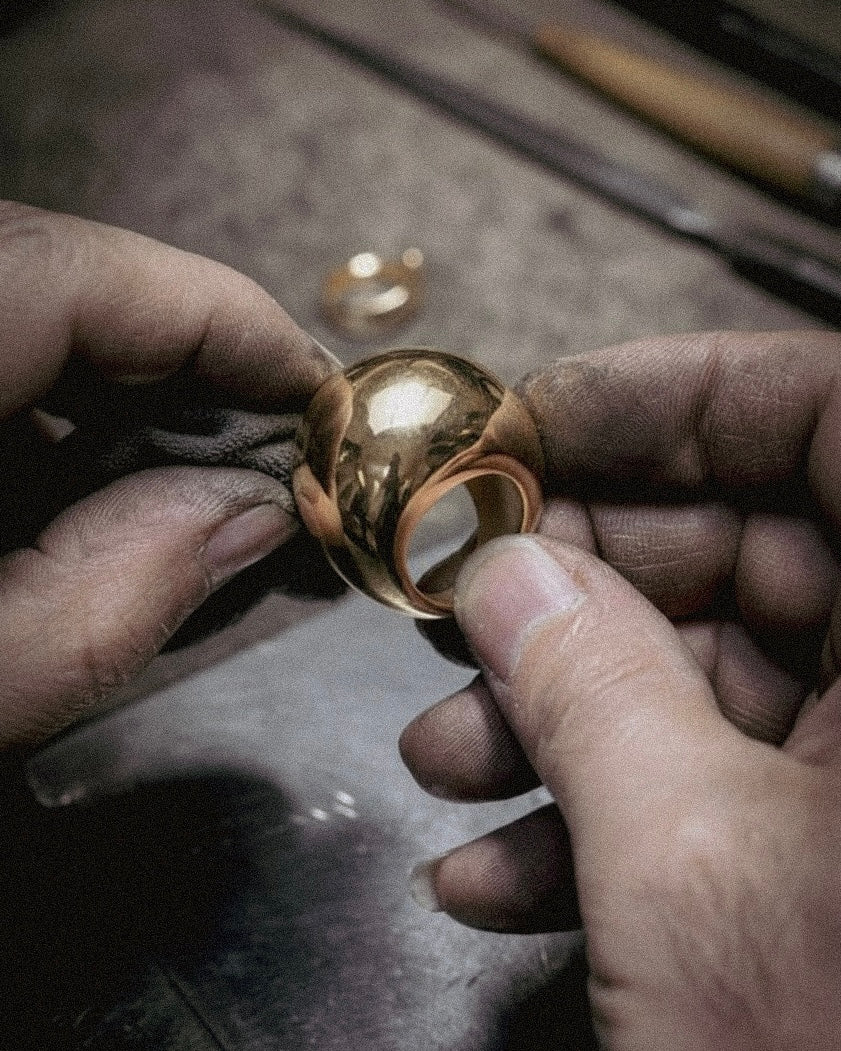 Gold ring being held and examined by a jeweler on a workshop bench.