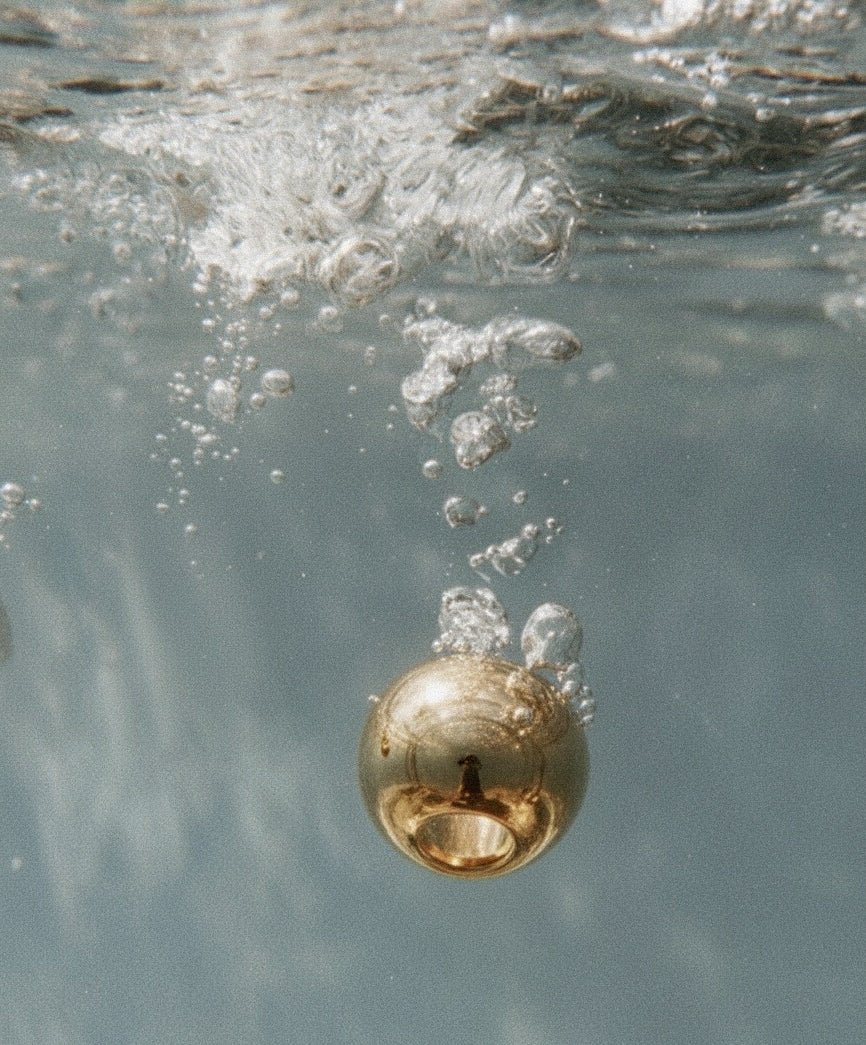 Gold ring ENSO DESIGN LAB by Ani Han submerged in water with bubbles around it
