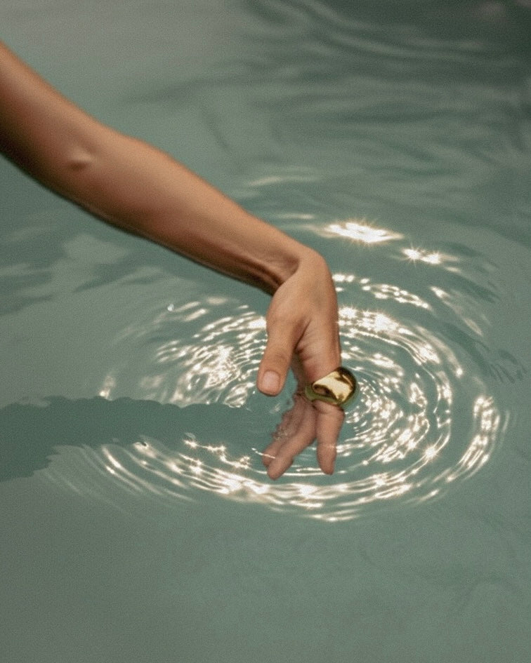 Hand with a gold ring touching water, creating ripples.