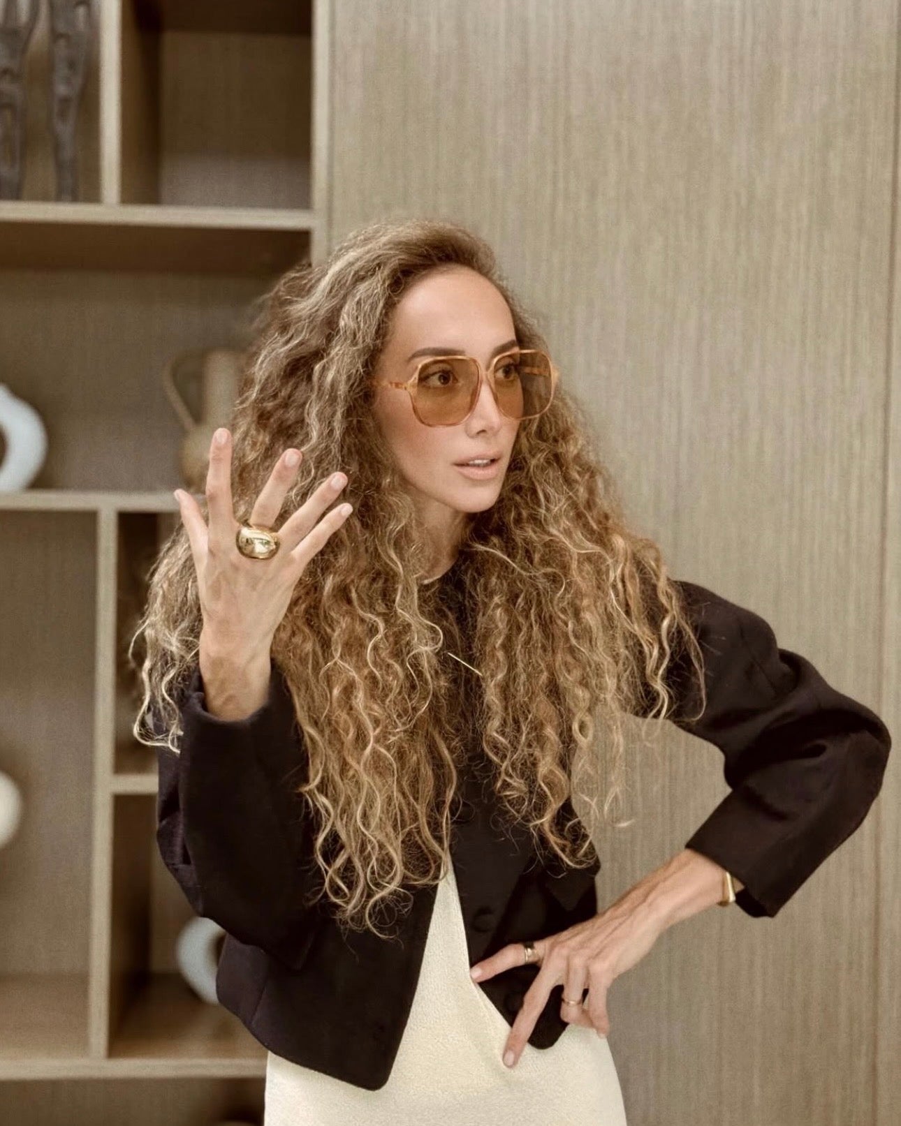 Ani Han speaking in the Enso studio, one hand raised to show a sculptural gold ring, wearing oversized amber sunglasses.