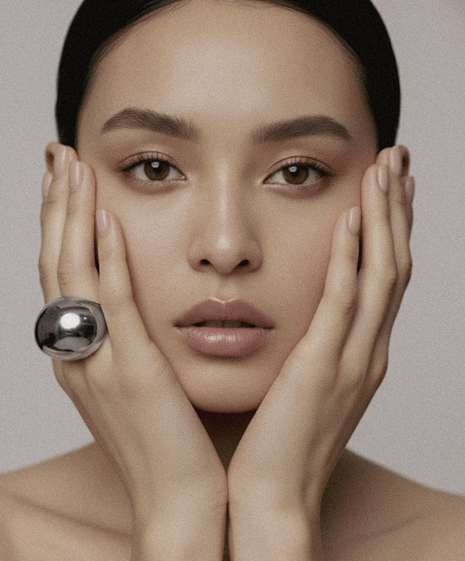 Model wearing silver-plated Flow Ring sculptural jewelry by Enso Design Lab, hands framing face to showcase statement piece
