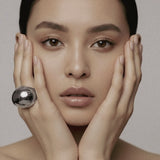 Model wearing silver-plated Flow Ring sculptural jewelry by Enso Design Lab, hands framing face to showcase statement piece
