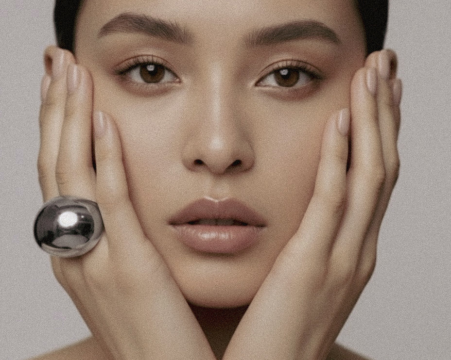 Model wearing silver-plated Flow Ring sculptural jewelry by Enso Design Lab, hands framing face to showcase statement piece
