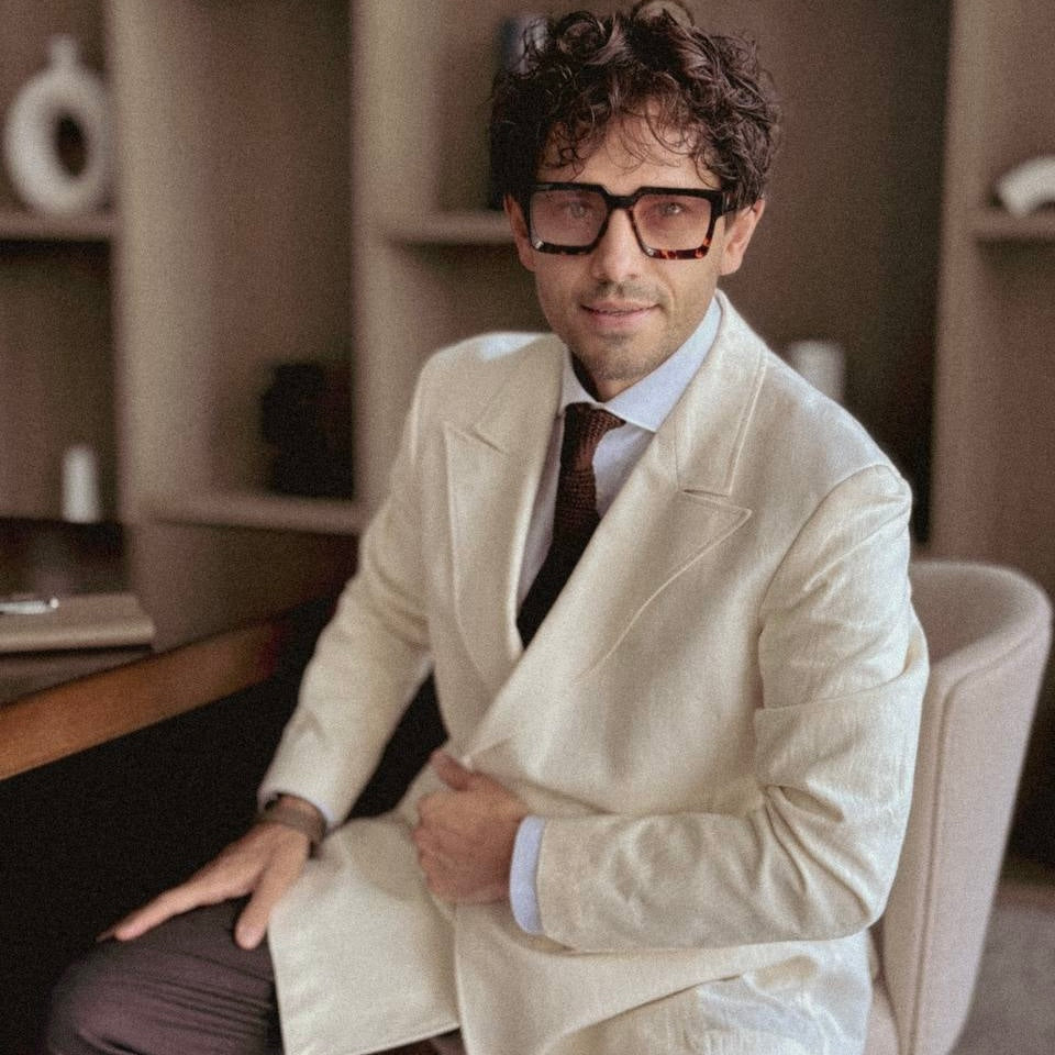 Bulat Han in a beige suit sitting in a room with shelves in the background