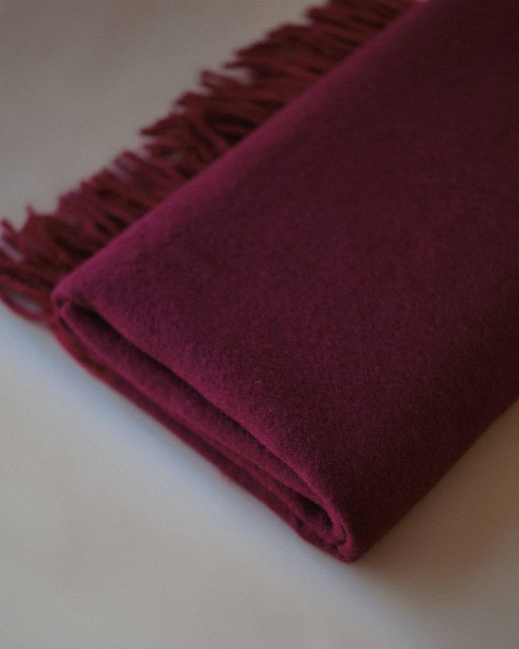 Close-up of a premium cashmere scarf in burgundy, showcasing its fine texture and hand-finished fringes by Enso Design Lab™.