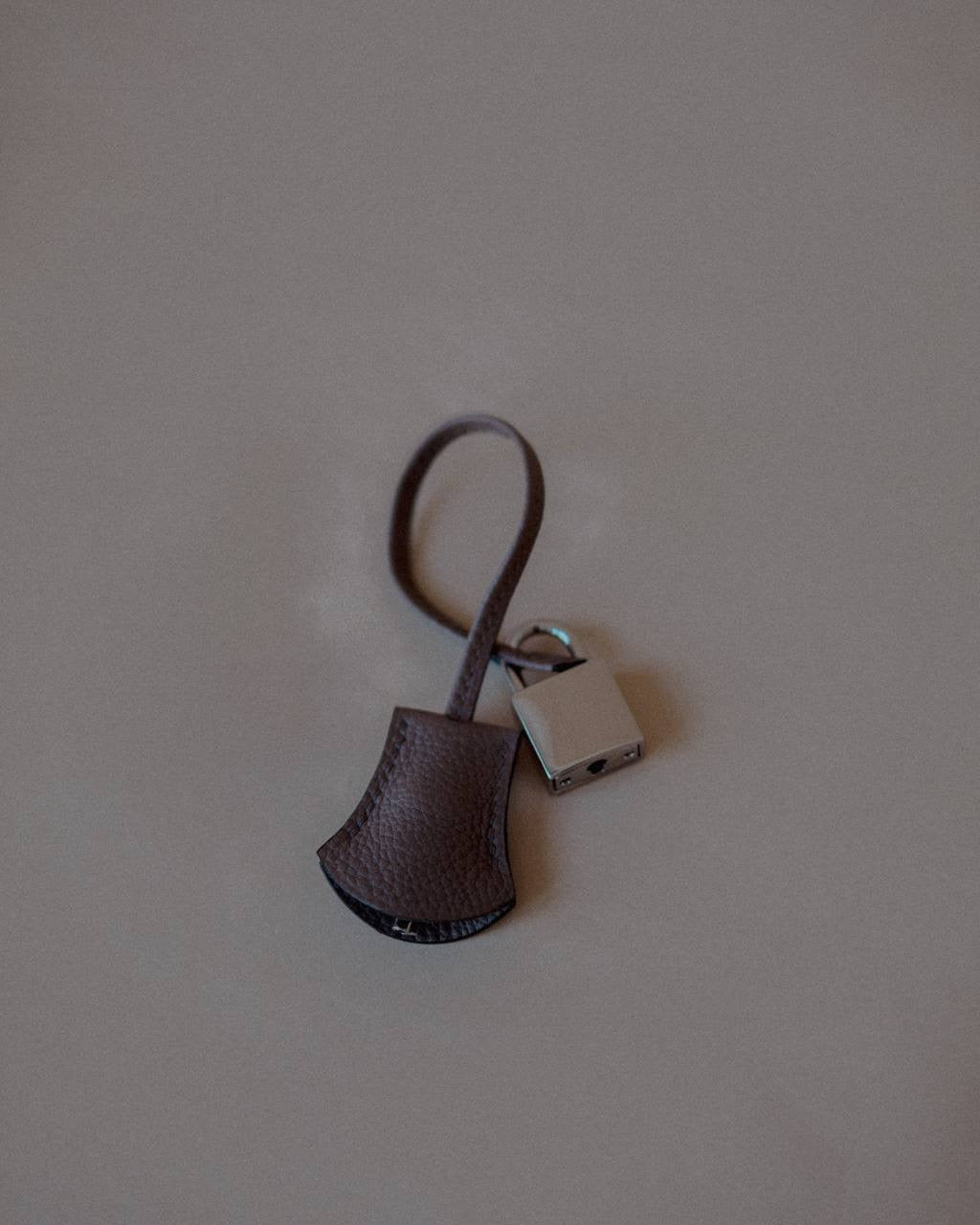 Side view of the Grey Leather Key Charm, highlighting its decorative padlock and smooth Swift Leather texture.