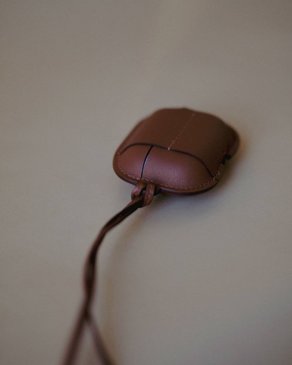 Golden Brown Leather AirPods Case Necklace displayed alongside a complementary Slate Mirage color, reflecting the elegance envisioned by Creative Director Ani Han.