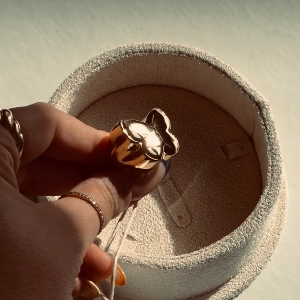 Jessica Issam (@jessicabarakat25) is holding up a large, elegantly designed gold ring from the Metamorphosis collection by Enso Design Lab. She’s pictured through a circular opening, adding an artistic and creative perspective to the shot.