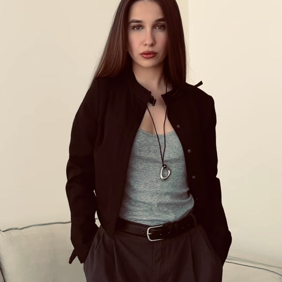 Portrait of Anastasia (@xfloresls), looking directly at the camera with confidence, wearing a striking necklace by Enso Design Lab. She is dressed in a smart gray blazer and black top, representing the sophistication and attention to detail that Enso Design Lab stands for.