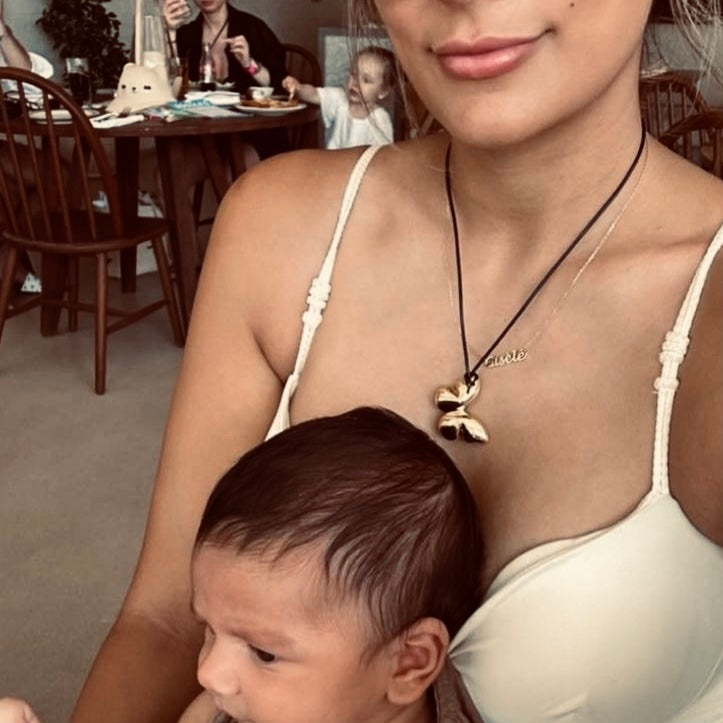 Sonia West (@sonia__west__) smiles warmly while holding her young child, both dressed in casual attire. She wears a simple yet elegant silver necklace that complements her look, showcasing the timeless and meaningful jewelry by Enso Design Lab.