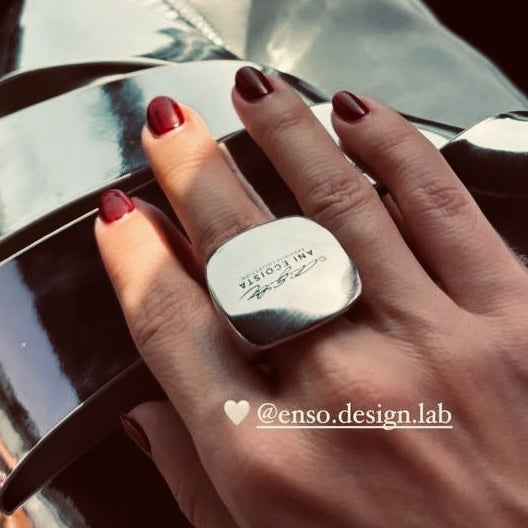 Elina Belkova (@elina_belkova) holds a uniquely designed silver ring from Enso Design Lab, prominently featuring the logo on the top. Her nail art and the ring’s modern aesthetic complement each other, highlighting both style and branding.