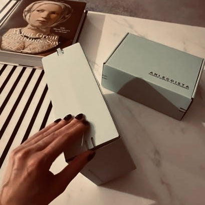 Elena (elena_shifrina) opens an elegant package from Enso Design Lab on a marble table next to a book about great women’s style.