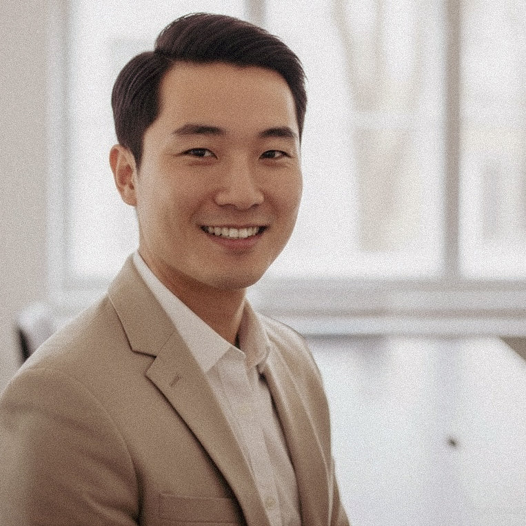 Man wearing a beige suit in an indoor setting with a blurred background
