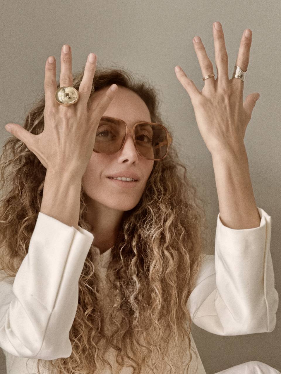 Ani Han wearing sunglasses with her hands raised showing off rings on a neutral background