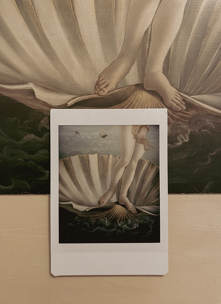 Framed artwork of a classical scene with draped figures on a wooden surface.
Shell Cuff bracelet on hand showing sculptural volume and fit