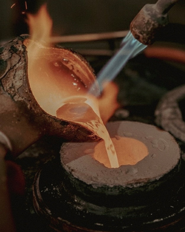Butter being poured onto a hot griddle with flames in the background. Workshop scene: crafting Shell Cuff with traditional metalworking tools