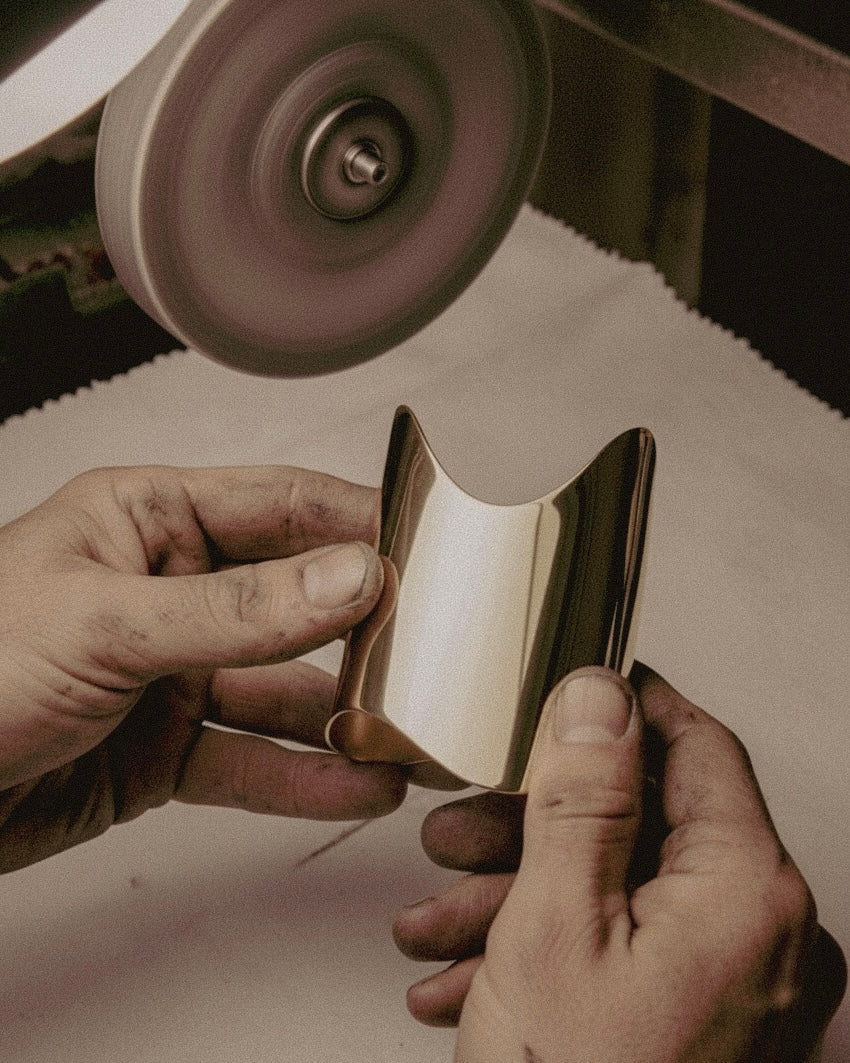 Person polishing a metallic object with a grinding wheel. Artisan pouring molten brass for Shell Cuff bracelet production